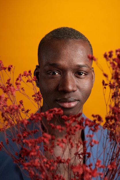 Gros plan sur un jeune homme africain regardant la caméra à travers les fleurs séchées sur fond jaune