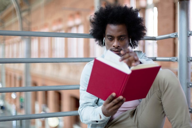 Gros plan sur un jeune homme afro-américain lisant un livre dans un lieu public Passe-temps et modes de vie sains Espace pour le texte