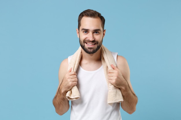 Gros plan jeune homme barbu de 20 ans en chemise blanche tenir une serviette sur les épaules isolé sur fond bleu pastel portrait en studio. Concept de procédures cosmétiques de soins de la peau. Maquette d'espace de copie