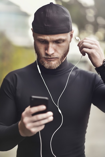 Gros plan d'un jeune homme blanc à la barbe mettant un casque dans son oreille. Un sportif déterminé est prêt pour la course longue distance et l'entraînement Athlète portant un tracker de fitness sportif et des écouteurs.