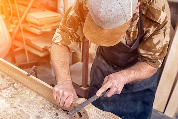 Gros plan sur un jeune homme constructeur portant une chemise à carreaux traitant un produit en bois avec un ciseau dans le gros plan de l'atelier