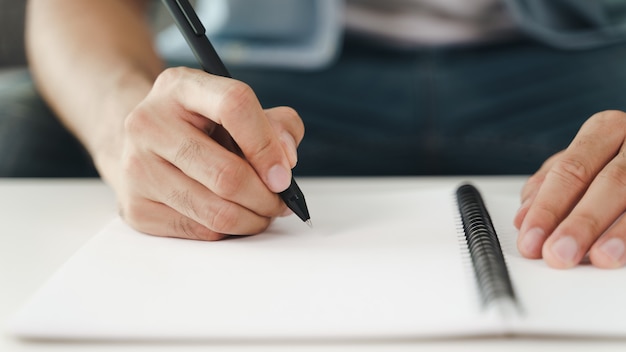 Gros Plan D'un Jeune Homme Dans Des Mains En Tissu Décontracté écrivant Sur Le Bloc-notes, Bloc-notes à L'aide D'un Stylo à Bille Sur La Table.