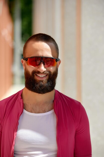 Gros plan d'un jeune homme européen séduisant et heureux avec une barbe portant des lunettes et des vêtements de sport roses regardant la caméra pendant la soirée dans le parc le week-end