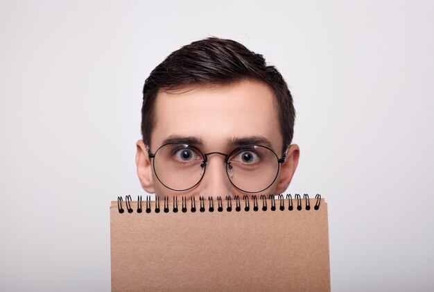 Un gros plan d'un jeune homme avec des lunettes furtivement derrière un ordinateur portable.