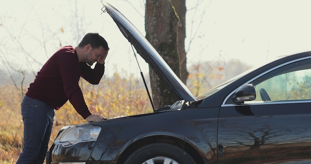 Gros plan, un jeune homme sort de la voiture et ouvre le capot pour vérifier le problème de la voiture cassée. Accident de la route de concept. Aide à la réparation.