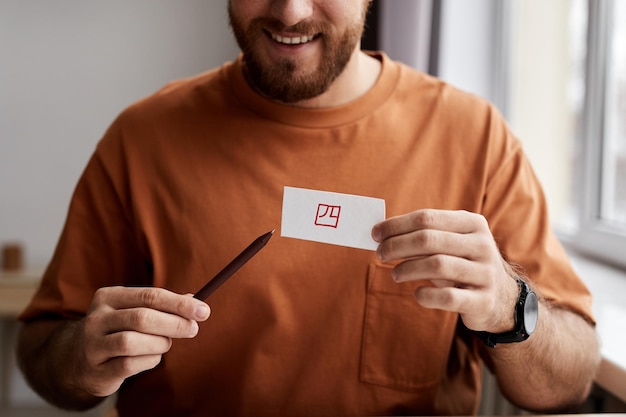 Gros plan d'un jeune homme souriant montrant une carte papier avec un hiéroglyphe écrit avec un surligneur rouge et une exp