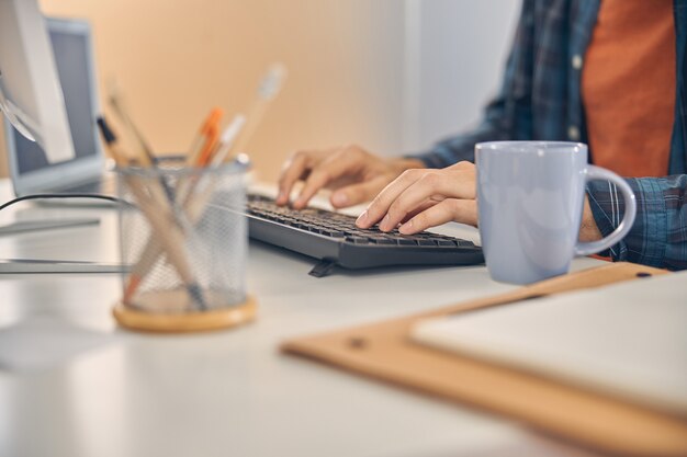 Gros plan d'un jeune homme utilisant un ordinateur de bureau alors qu'il était assis à table avec une tasse de café