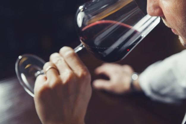 Gros plan d'un jeune sommelier sentant le vin rouge sur fond de comptoir de bar