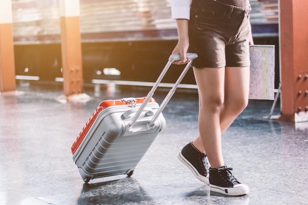 Gros plan sur une jeune touriste voyageuse portant son sac rouge chariot et sa carte dans une gare, concept de voyage de vacances.