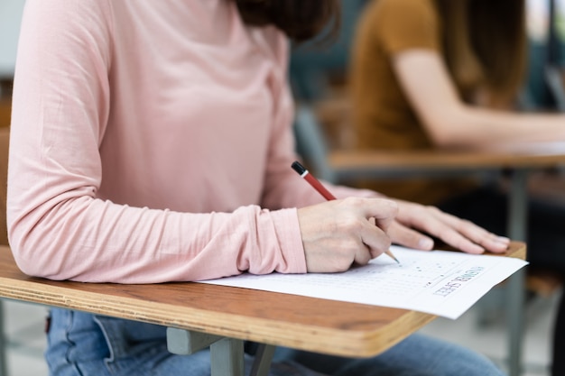 Gros plan sur de jeunes étudiantes universitaires se concentrant sur l'examen en classe. Une étudiante écrit la réponse des examens sur une feuille de réponses dans la salle de classe.