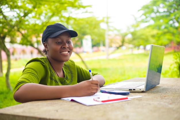 Gros plan sur une jolie étudiante africaine excitée alors qu'elle travaille sa mission sur le campus