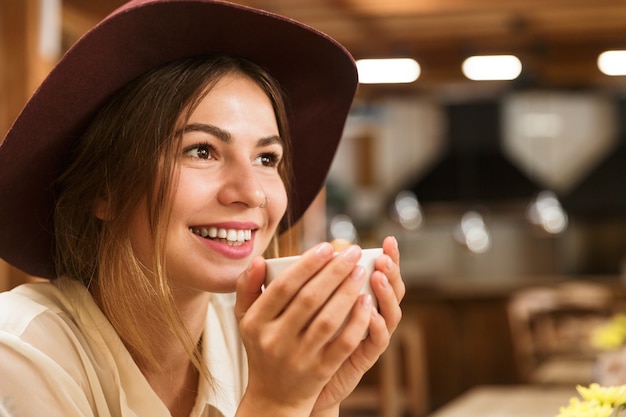 Gros plan d'une jolie femme au chapeau assis à la table du café