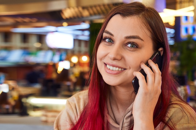 Gros plan de jolie femme aux longs cheveux roux parlant sur un téléphone portable dans un café