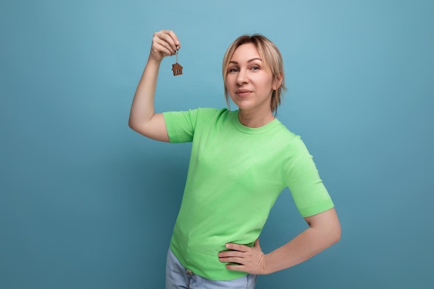 Gros plan d'une jolie femme blonde chanceuse au look décontracté tenant un porte-clés d'appartement sur fond bleu