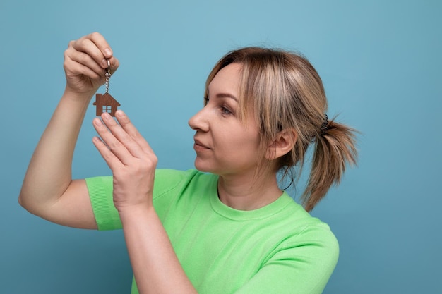 Gros plan d'une jolie fille blonde joyeuse et joyeuse dans un look décontracté qui montre l'achat d'une maison sur un bleu