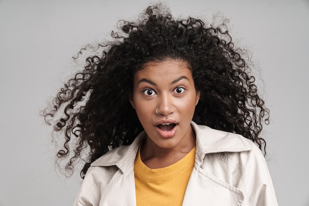 Gros plan d'une jolie jeune femme africaine choquée aux cheveux bouclés, portant un manteau d'automne