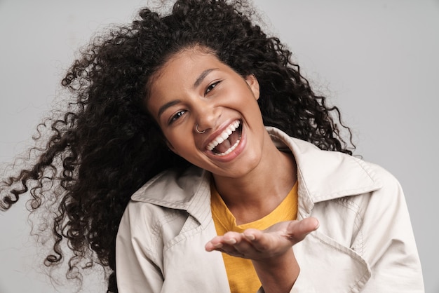 Gros plan d'une jolie jeune femme africaine souriante aux cheveux bouclés, portant un manteau d'automne