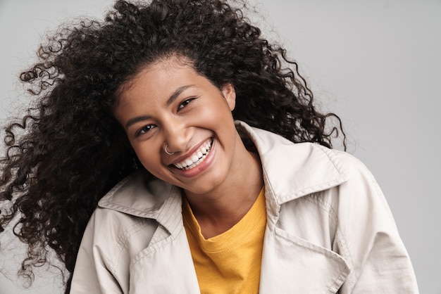 Gros plan d'une jolie jeune femme africaine souriante aux cheveux bouclés, portant un manteau d'automne