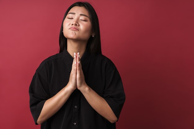 Gros plan d'une jolie jeune femme asiatique portant des vêtements décontractés, isolé sur un mur rouge, mendiant