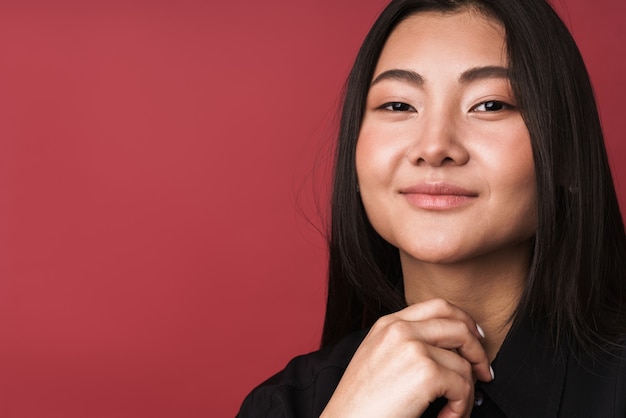 Photo gros plan d'une jolie jeune femme asiatique souriante portant des vêtements décontractés, isolée sur un mur rouge, regardant la caméra