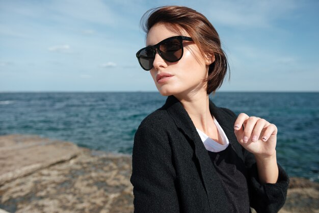 Gros plan d'une jolie jeune femme à lunettes de soleil marchant près de la mer