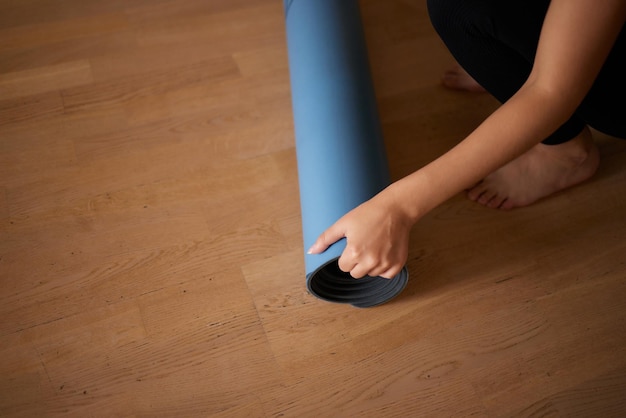 Gros plan d'une jolie jeune femme posant un tapis de yoga ou de fitness bleu avant de faire de l'exercice en studio