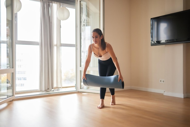 Gros plan d'une jolie jeune femme posant un tapis de yoga ou de fitness bleu avant de faire de l'exercice en studio