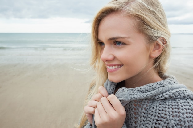 Gros plan d&#39;une jolie jeune femme souriante en veste grise en tricot sur la plage