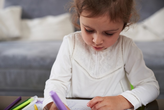 Gros plan d'une jolie petite fille en chemise blanche dessin avec des crayons de couleur à la maison