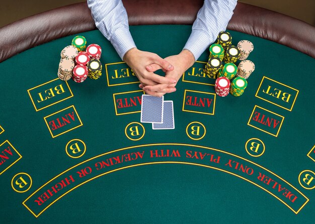 Gros plan sur un joueur de poker avec des cartes à jouer et des jetons à la table de casino verte, vue d'en haut.