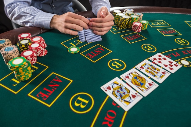 Gros plan sur un joueur de poker avec des cartes à jouer et des jetons à la table de casino verte