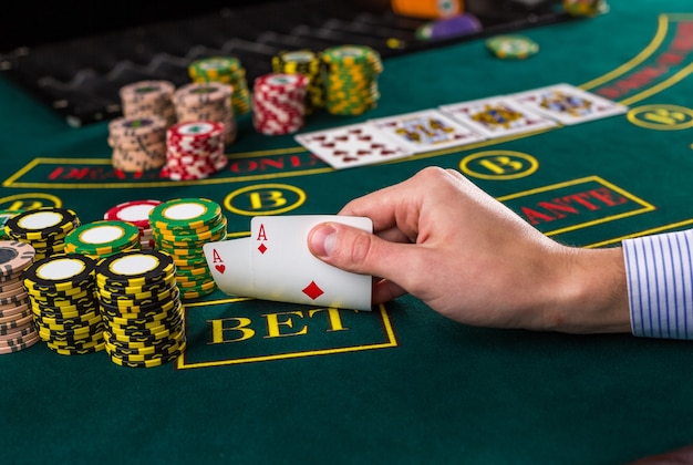 Gros plan sur un joueur de poker masculin soulevant les coins de deux cartes as à la table de casino verte avec as