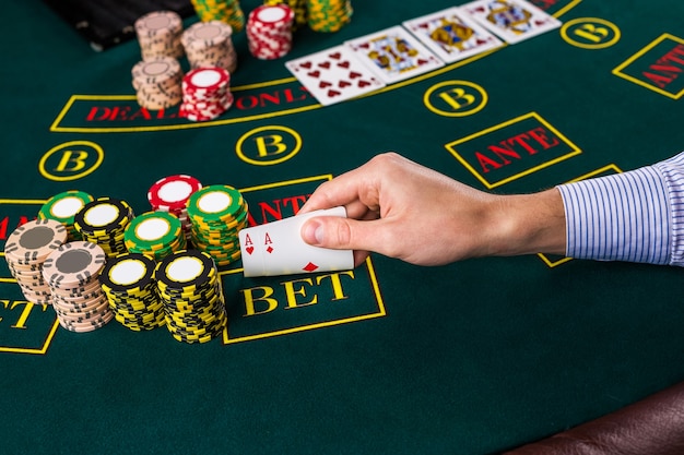 Gros plan sur un joueur de poker masculin soulevant les coins de deux cartes as à la table de casino verte avec as