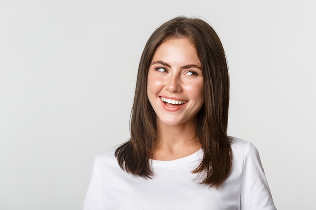 Gros plan de joyeuse belle fille brune regardant à droite et riant heureux, blanc.