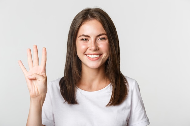 Gros plan de joyeuse jolie jeune femme souriante, montrant quatre doigts, blanc.