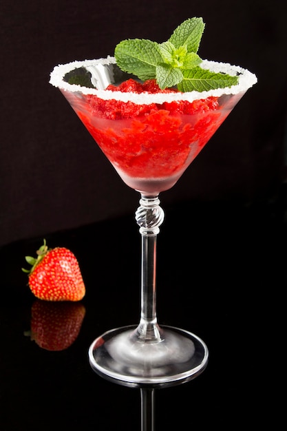 Gros plan sur le jus congelé à la fraise dans le verre à martini sur le tableau noir.