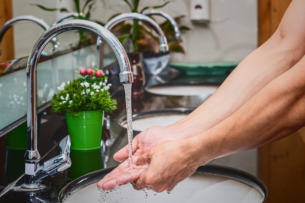 Gros plan sur le lavage des mains avec un robinet chromé et de l'eau pour la pandémie de coronavirus