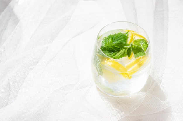 Gros plan de limonade maison avec de la menthe citronnée et des glaçons dans un verre sur une table en bois blanc avec un tissu en tulle blanc