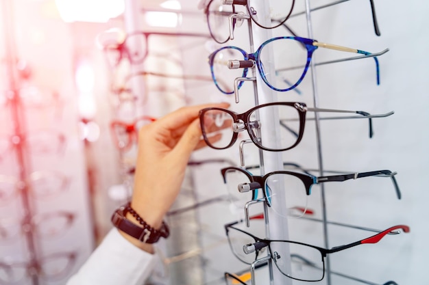 Gros plan de lunettes Femme à lunettes Choisir des lunettes Client en optique Mise au point sélective Femme avec des lunettes dans les mains Stand avec des lunettes Large assortiment dans la boutique