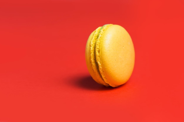 Gros plan d'un macaron sucré jaune sur fond rouge. Pâtisseries françaises sucrées pour le thé. Espace de copie