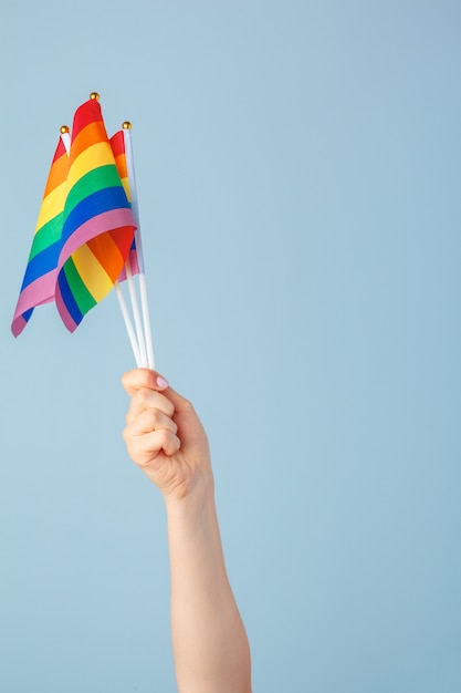 Gros plan d'une main en agitant un petit drapeau arc-en-ciel sur un fond bleu clair