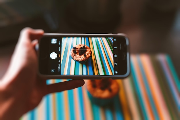 Gros plan de la main à l'aide d'un téléphone portable tout en photographiant un muffin