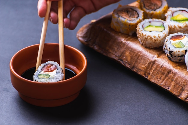 Gros plan de la main avec des baguettes trempant des sushis dans de la sauce soja