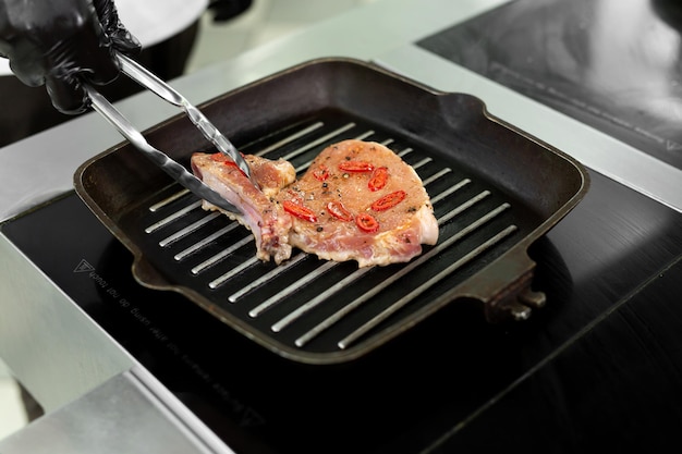 Gros plan sur la main d'un chef tenant une poêle à griller avec des steaks et des légumes grillés.