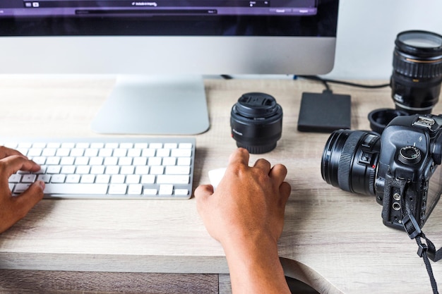 Gros plan de la main d'un concepteur éditant une photo sur un ordinateur dans un appareil photo et des objectifs professionnels de bureau