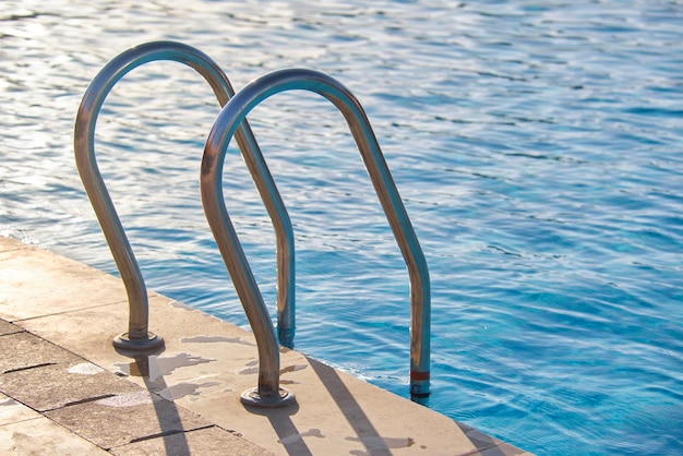 Gros plan de la main courante en acier inoxydable de la piscine descendant dans l'eau de la piscine claire comme une tortue. Concept d'accessibilité des activités récréatives.
