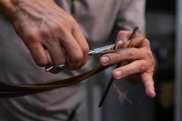 Gros plan de la main du coiffeur prenant les cheveux de la femme pour la coupe Main du coiffeur avec une brosse à ciseaux sur le lieu de travail Concept de service de salon de beauté Mise au point sélective