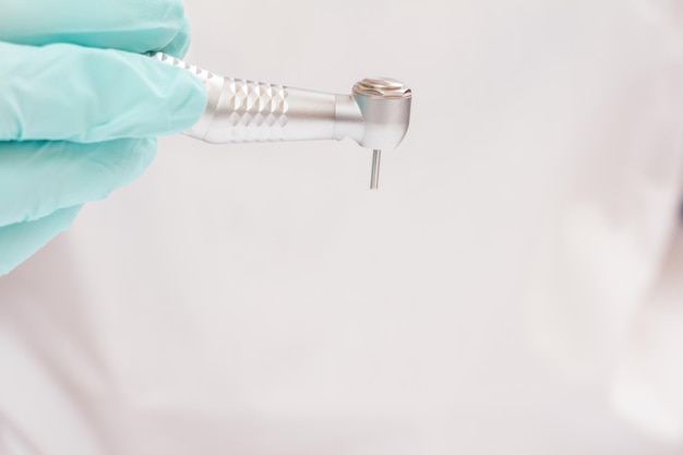 Gros plan de la main du dentiste dans un gant en latex avec pièce à main dentaire à grande vitesse sur fond flou