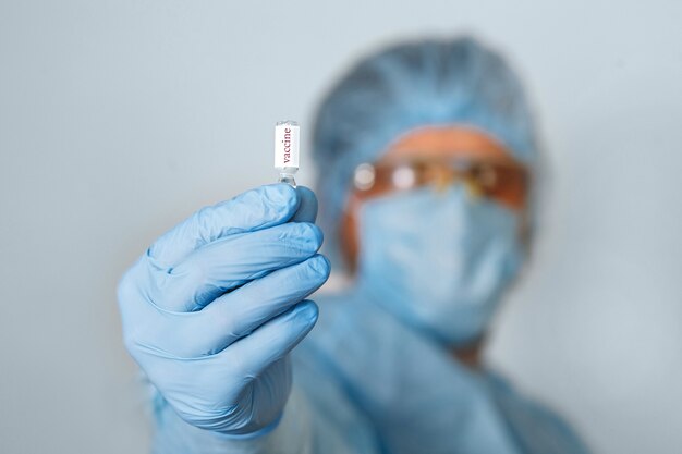 Gros plan de la main du médecin tenant le vaccin. Équipement médical. Un médecin portant un équipement de protection individuelle comprenant un masque, des lunettes et une combinaison pour protéger l'infection par le coronavirus COVID 19.