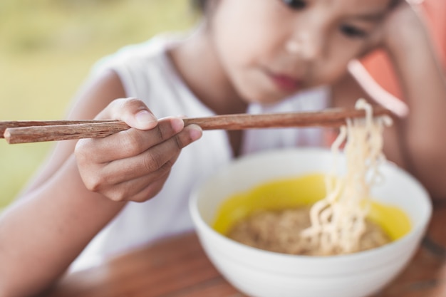 Gros plan sur la main de l&#39;enfant fille tenant des baguettes pendant qu&#39;elle mange des nouilles instantanées